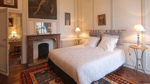 A bedroom with a large bed, a fireplace, and a painting on the wall.
