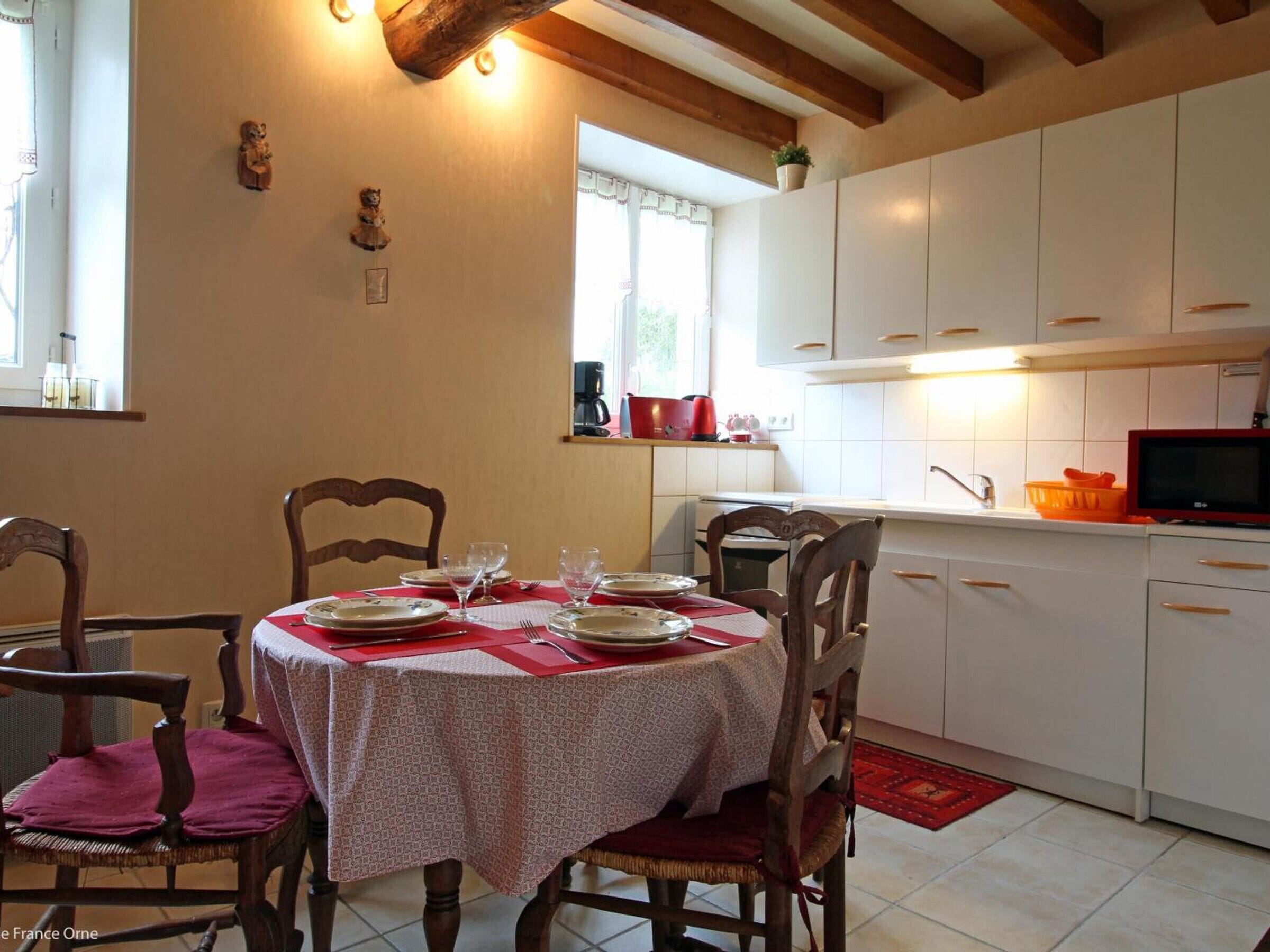 Un coin repas avec une table ronde dressée pour quatre personnes, des chaises en bois et un tapis rouge.