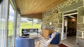 A cozy room with a stone wall, a wooden ceiling, and a large window overlooking a green landscape.