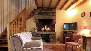 A cozy living room with a stone fireplace, wooden staircase, and a television on a wooden stand.