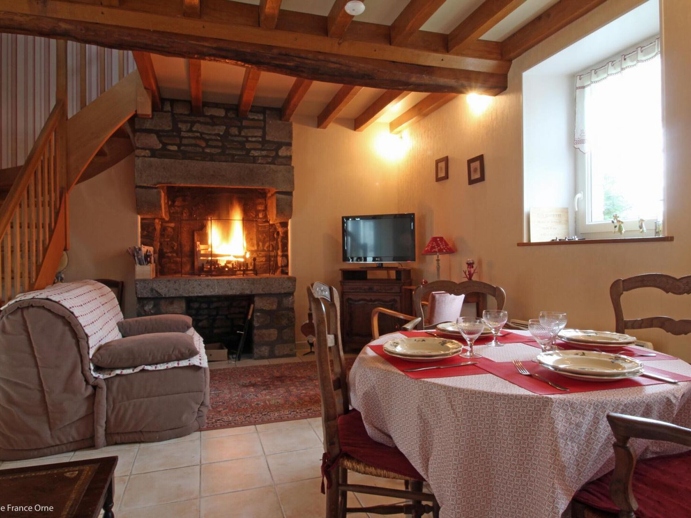 Ein gemütliches Wohnzimmer mit Kamin aus Stein, einem Esstisch für zwei Personen und einem Fernseher auf einem Holzboden.