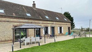 Un bâtiment à l’extérieur en briques, doté d’un espace extérieur abrité avec des tables et des chaises, et d’une pelouse verdoyante à l’avant.