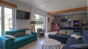 Un salon avec un canapé turquoise, un canapé bleu foncé, une table basse blanche, un téléviseur fixé au mur et un jeu de fléchettes.