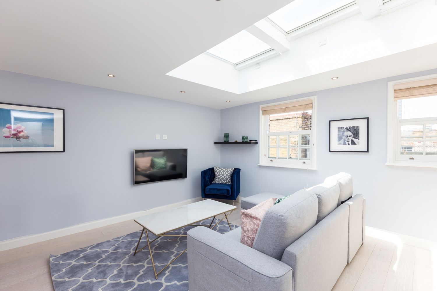 A modern living room with a flat-screen TV, a blue armchair, a grey sofa, and a patterned rug.
