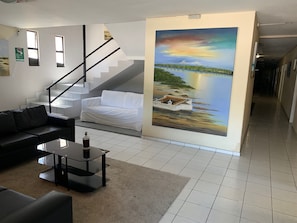 A modern living room with a staircase, a white sofa, a black leather couch, and a painting of a bridge over water. - CP Hotel (Natal)