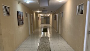 A long, narrow hallway with beige walls and white tiled floors. There are doors on both sides, and a rug runs down the center. - CP Hotel (Natal)
