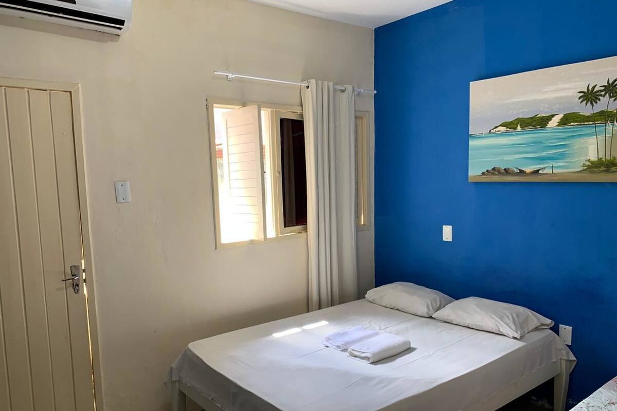 A bedroom with a bed, a window with curtains, a painting on the wall, and a door.