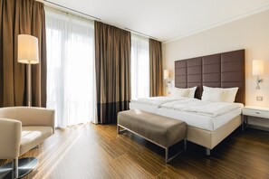 Una habitación de hotel con una cama grande, mesitas de noche, una silla y un banco.