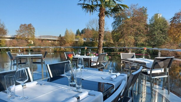 An outdoor dining area with tables set for two, overlooking a body of water and surrounded by trees. - Hotel Eberhards am Wasser (Bietigheim-Bissingen)