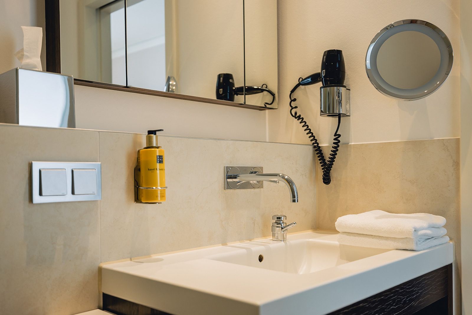 A bathroom with a white sink, a mirror, a hairdryer, and a bottle of shampoo.