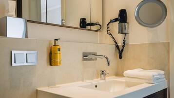 A bathroom with a white sink, a mirror, a hairdryer, and a bottle of shampoo.