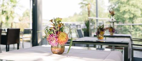 Una mesa de comedor con un jarrón de flores, en un espacio interior luminoso con ventanas amplias.