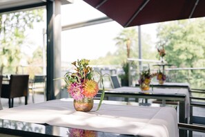 Una mesa de comedor con un jarrón de flores, en un espacio interior luminoso con ventanas amplias.