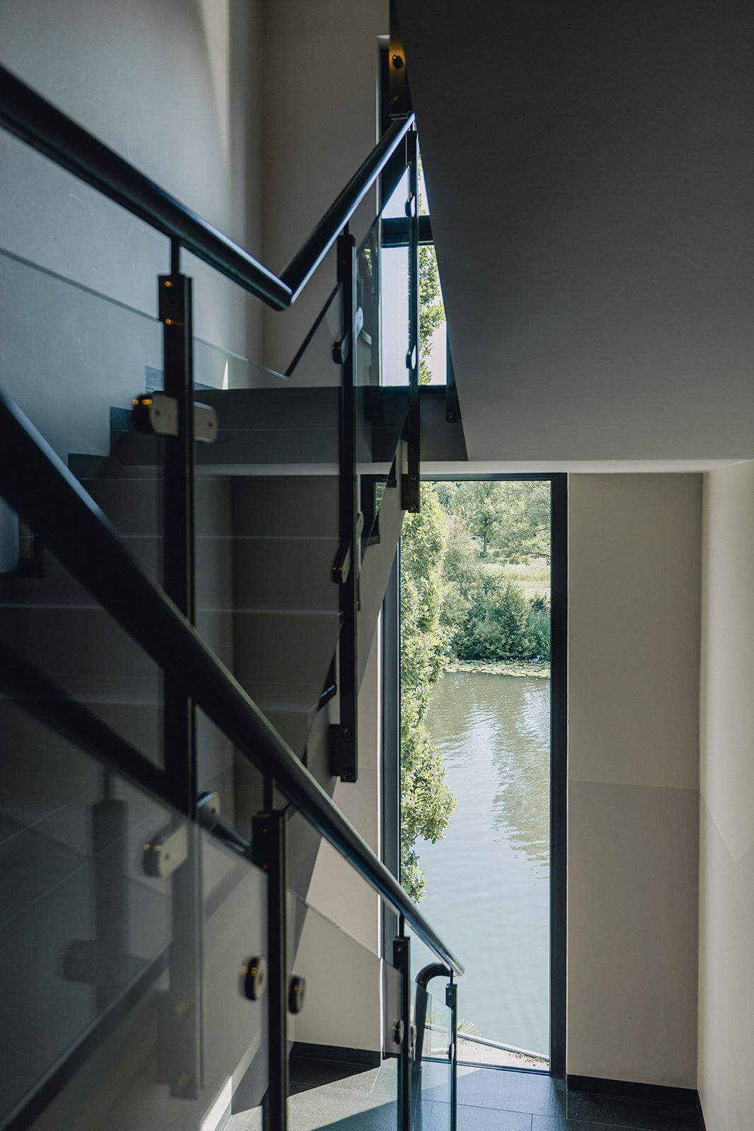Una escalera moderna con barandas de vidrio que conduce a una puerta con vista al río.
