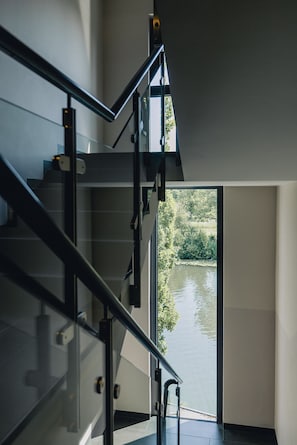 A modern staircase with glass railings leading to a door with a view of a river. - Hotel Eberhards am Wasser (Bietigheim-Bissingen)