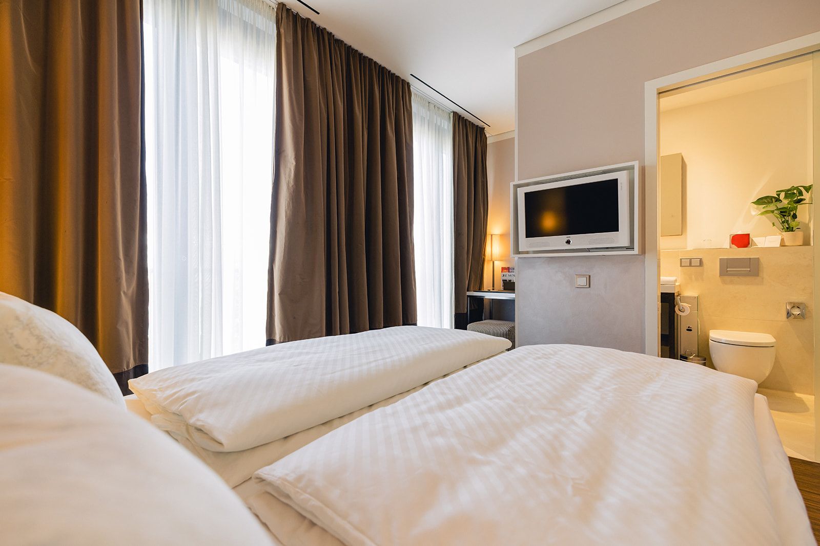 A hotel room with two beds, a television, a bathroom, and a window with curtains.
