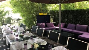 An outdoor dining area with tables set for a meal, surrounded by greenery and a cushioned seating area. - Hotel Eberhards am Wasser (Bietigheim-Bissingen)