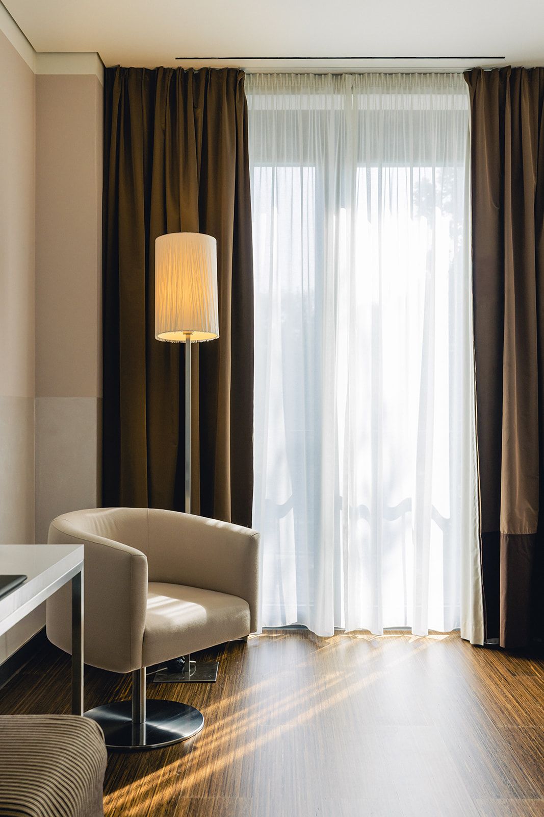 Ein Hotelzimmer mit einer Couch, einer Lampe und Blick durch durchsichtige Vorhänge.