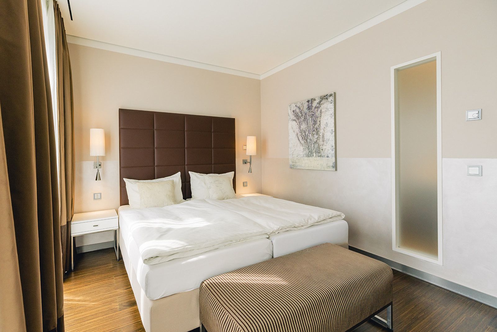 Quarto de hotel com cama grande, mesas de cabeceira, um banco e um quadro na parede.