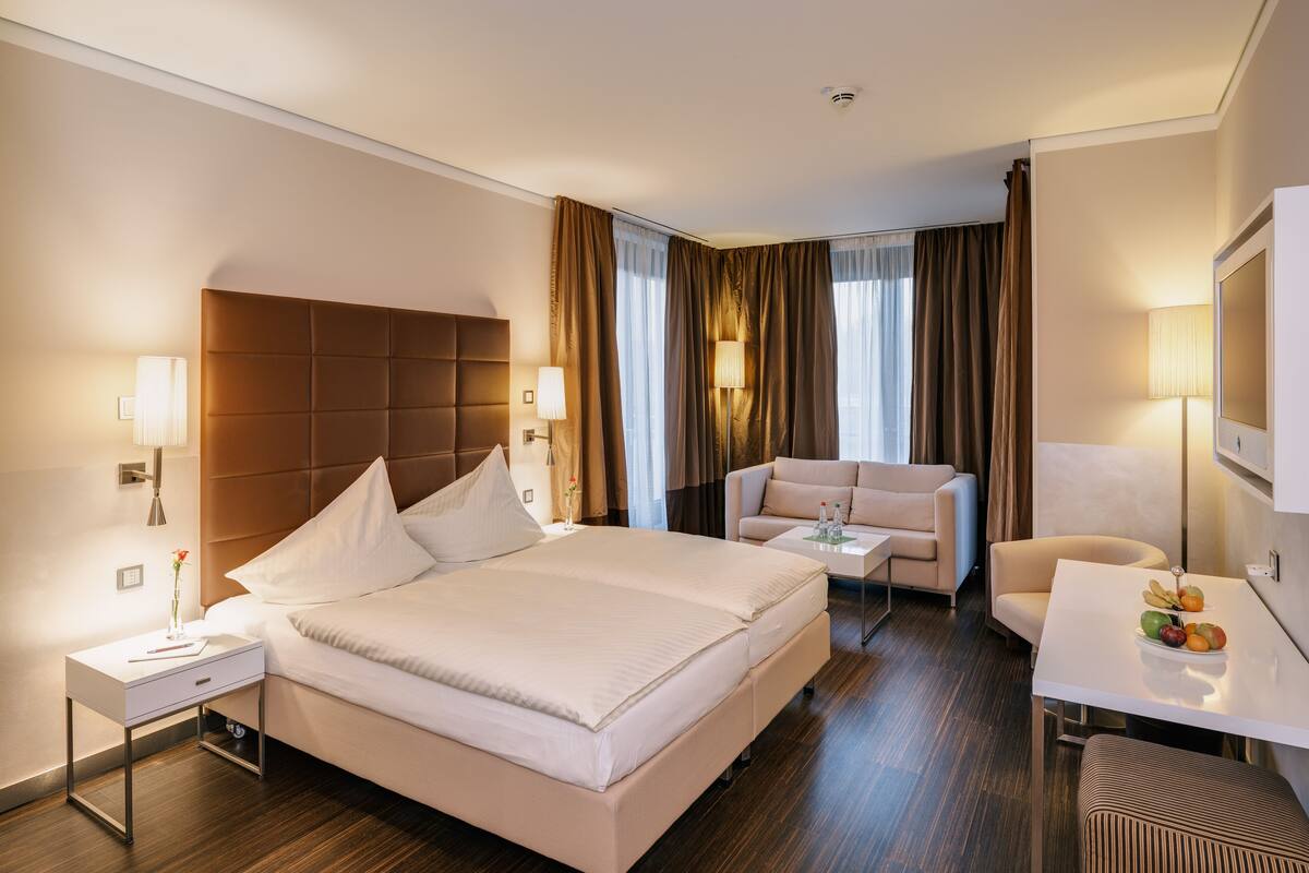 A hotel room with a large bed, a sofa, a small table with fruit, and a TV.