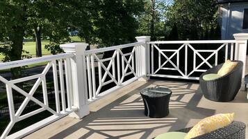 A balcony with white railings, wicker furniture, and a view of a green landscape.