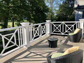 A balcony with white railings, wicker furniture, and a view of a green landscape. - Greenview Manor Luxury Bed & Breakfast (Niagara-on-the-Lake)