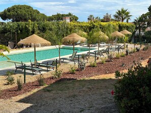 A pool area with lounge chairs and thatched umbrellas, surrounded by greenery and trees. - Apartment In Jardins do Golfe, Vale Do Lobo (Faro)