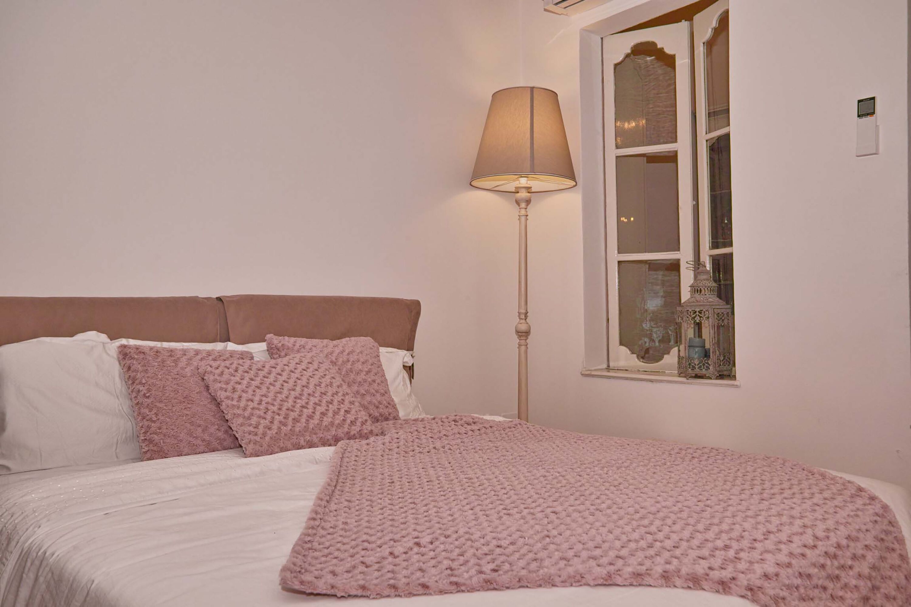 A bedroom with a bed, pillows, a lamp, and a window.