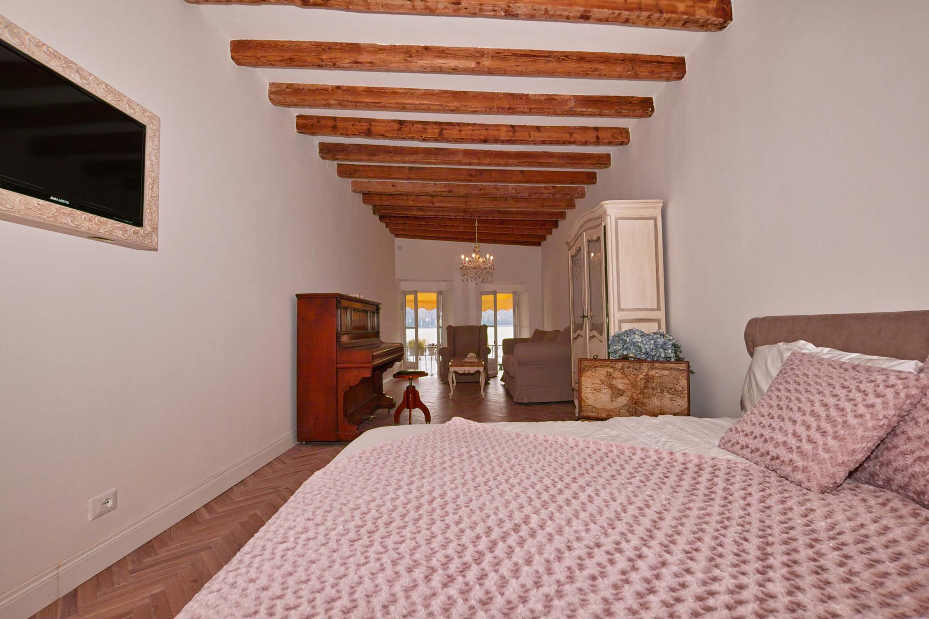 Ein Schlafzimmer mit einem großen Bett, Holzbalken an der Decke, einem Fernseher und Blick auf das Wohnzimmer.