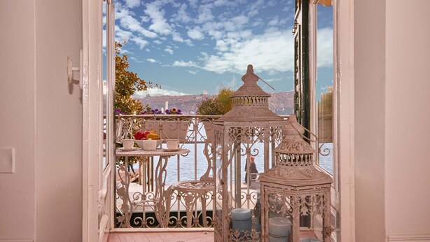 Un balcon orné de balustrades en métal blanc ouvragé, une petite table avec des fruits et une lanterne décorative.