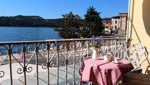 Un balcon avec une table dressée pour deux personnes, donnant sur une étendue d’eau et une colline.