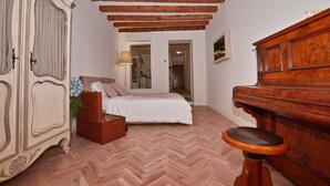 Une chambre à coucher avec un lit en bois, une commode, un piano et un parquet à motifs en chevrons.