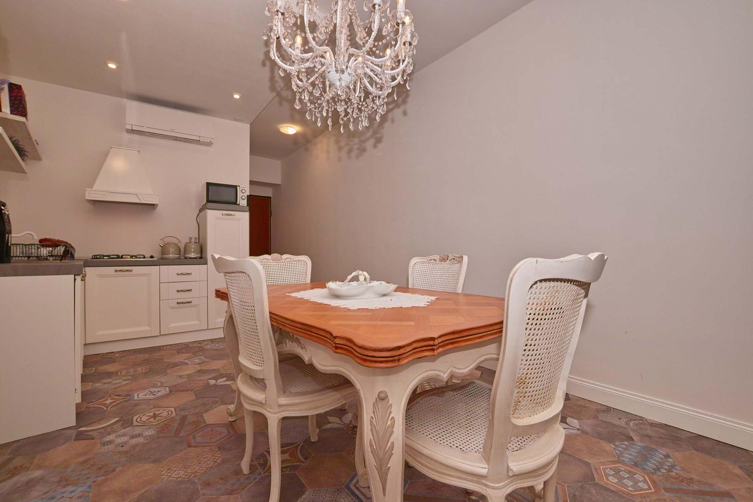 Un espace repas comprenant une table en bois, des chaises blanches, un lustre et des carreaux de sol à motifs.