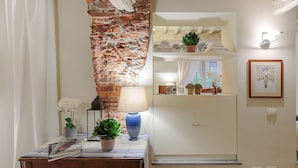 Una habitación con pared de ladrillo, un armario blanco, una mesa con lámpara y un cuadro en la pared.