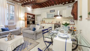 Una sala de estar acogedora con sofás a rayas, una mesa de comedor lista para una comida, y una cocina al fondo.