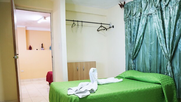 Une chambre d’hôtel avec deux lits, une armoire en bois, un porte-manteau et une salle de bain visible à travers une porte ouverte.