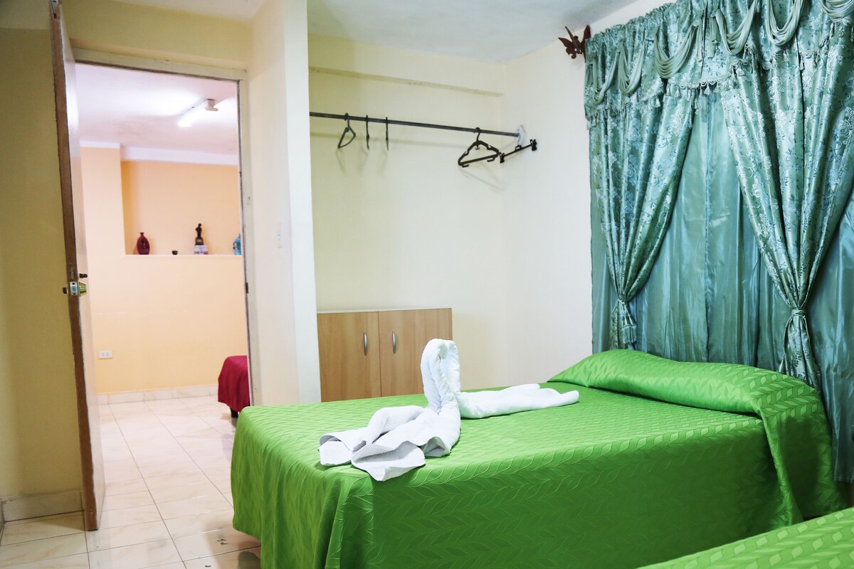A hotel room with two beds, a wooden wardrobe, a hanging coat rack, and a bathroom visible through an open door.