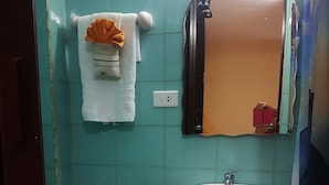 Une salle de bain avec un lavabo blanc, un porte-serviettes sur lequel sont posés un serviette blanche et une serviette orange, et un miroir dont le cadre est endommagé.