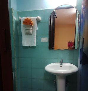 A bathroom with a white sink, a towel rack with a white towel and an orange towel, and a mirror with a damaged frame. - Casa Saymor (Havana)
