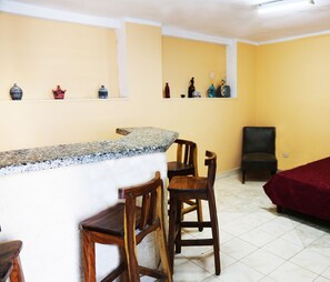 A room with a bar area, wooden chairs, a red bed, and shelves with decorative items. - Casa Saymor (Havana)