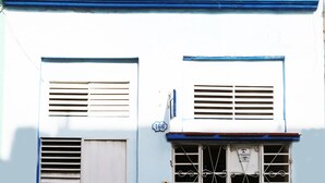 Un bâtiment à la façade bleue, doté de deux fenêtres avec volets, d’un portail en métal et d’une porte.