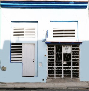 A building with a blue facade, two windows with shutters, a metal gate, and a door. - Casa Saymor (Havana)
