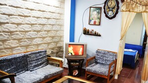 Un salon avec un canapé, un fauteuil et une table basse. Une télévision est posée sur un meuble et une horloge est accrochée au mur.
