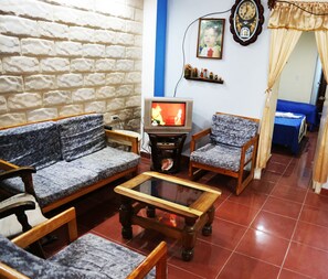 A living room with a sofa, armchair, and coffee table. A television is on a stand, and a clock is on the wall. - Casa Saymor (Havana)