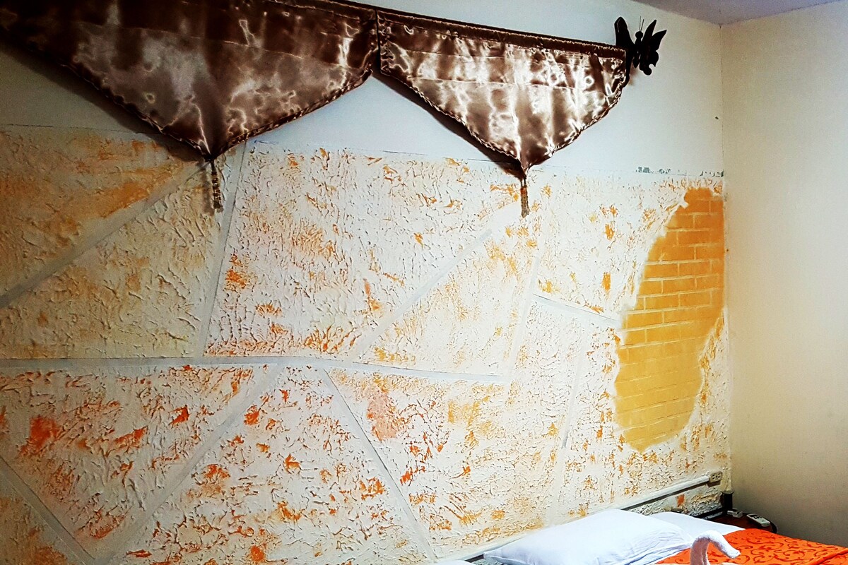 A room with a bed, pillows, a blanket, and a wall with a textured pattern.