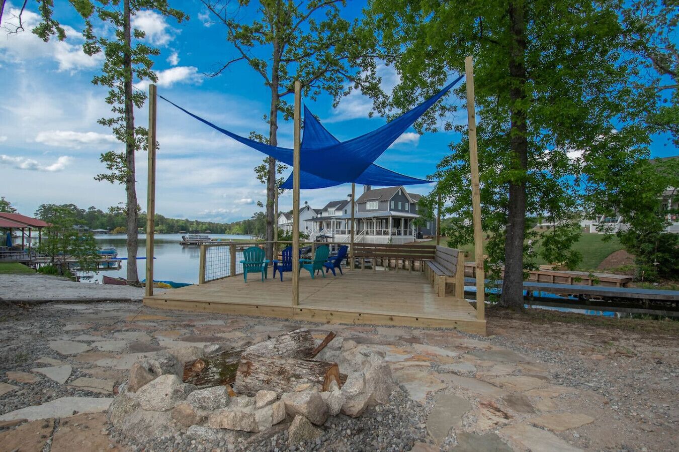A wooden deck with outdoor seating, overlooking a lake with a house in the background.