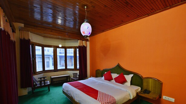 A hotel room with a wooden ceiling, a large bed with red and white bedding, a bench, and a window with curtains. - OYO 28187 Hotel Potala (Manali)