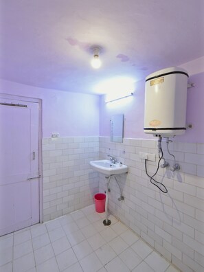 A bathroom with a white sink, a mirror, a toilet, a pink trash bin, and a water heater mounted on the wall. - OYO 28187 Hotel Potala (Manali)