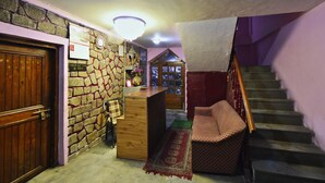 A room with a stone wall, a wooden door labeled "PRIVATE ROOM," a check-out time sign, a wooden counter, a checkered sofa, a staircase, and a hanging white cloth. - OYO 28187 Hotel Potala (Manali)