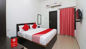 Habitación de hotel con una cama, una cortina roja, un televisor y un equipo de aire acondicionado.